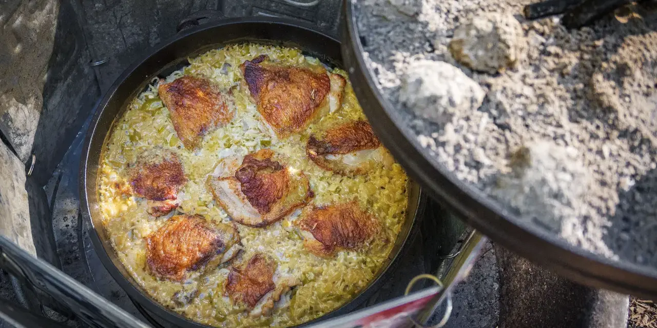 A delicious chicken and rice dish is cooking in a Dutch oven over a campfire, perfect for outdoor dutch oven campfire recipes.