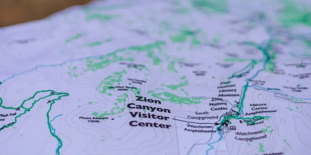 A topographic map of Zion Canyon shows elevation changes with contour lines, highlighting trails, visitor centers, and campgrounds.