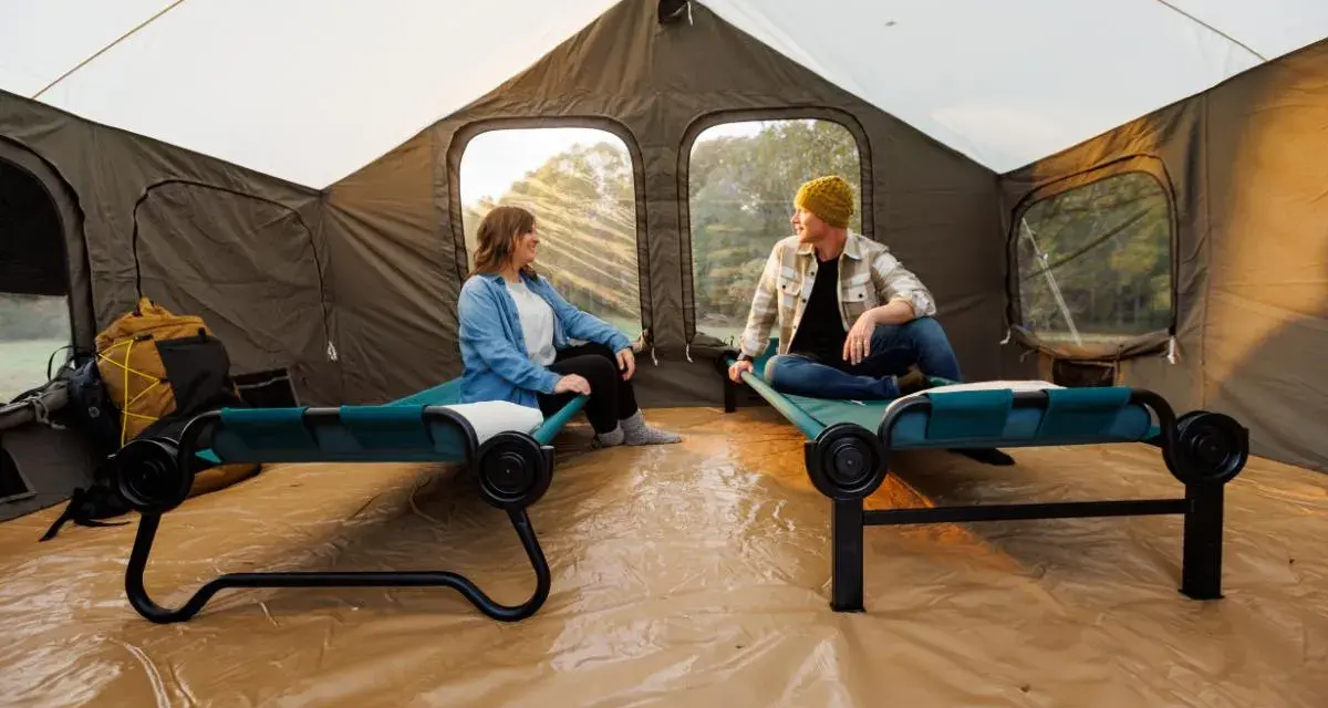 Two people relax on cots inside a large tent, showcasing smart tent camping hacks for comfort and organization.