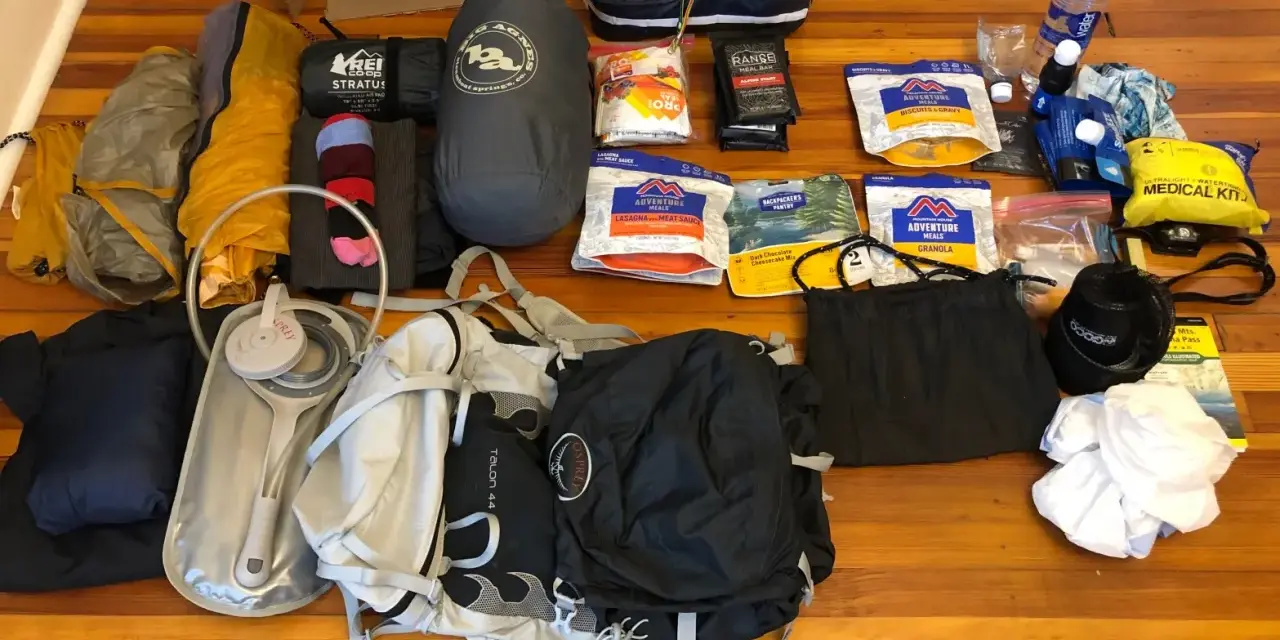 Gear laid out for beginner backpacking: tent, sleeping bag, backpack, water filter, food, and a medical kit.