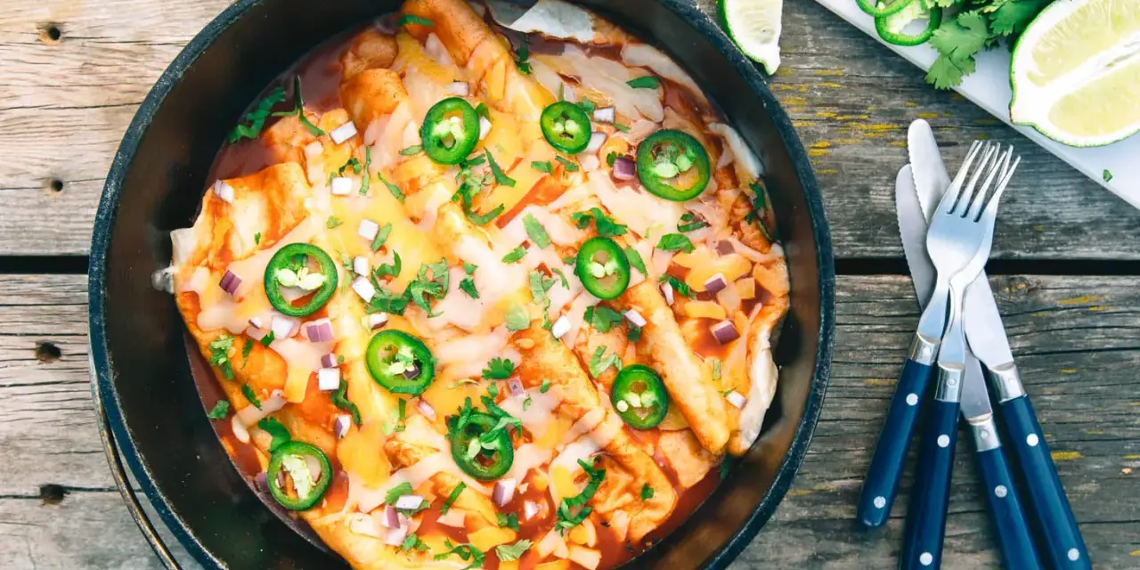 Delicious dutch oven enchiladas, topped with melted cheese, jalapeños, and cilantro, ready to be served.
