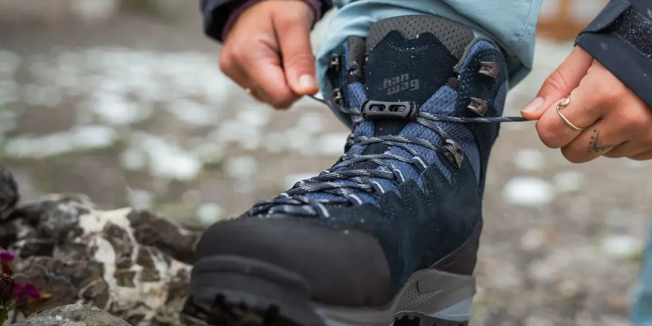 Hands tying laces on a new pair of Han Wag hiking boots, ready for breaking them in on the trail.
