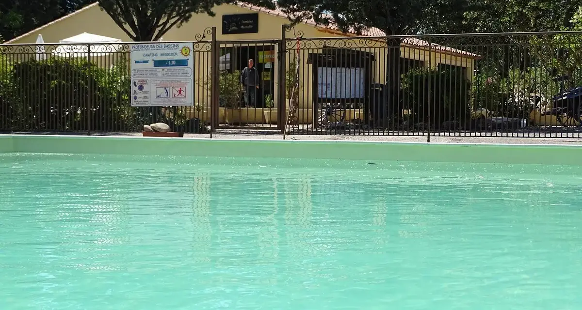 A refreshing pool awaits at this camping in Aix en Provence. A sign details pool depths, and a man stands near the reception building.