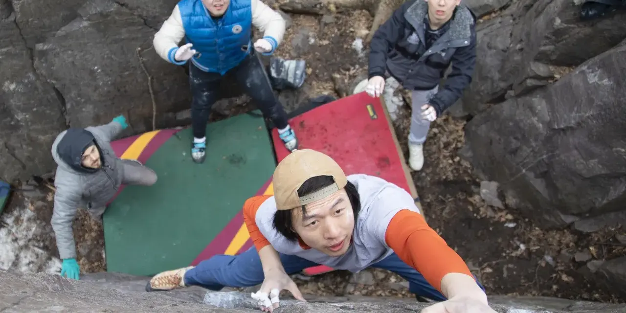 Four friends enjoy bouldering, a type of rock climbing, on a rocky outdoor course with crash pads.