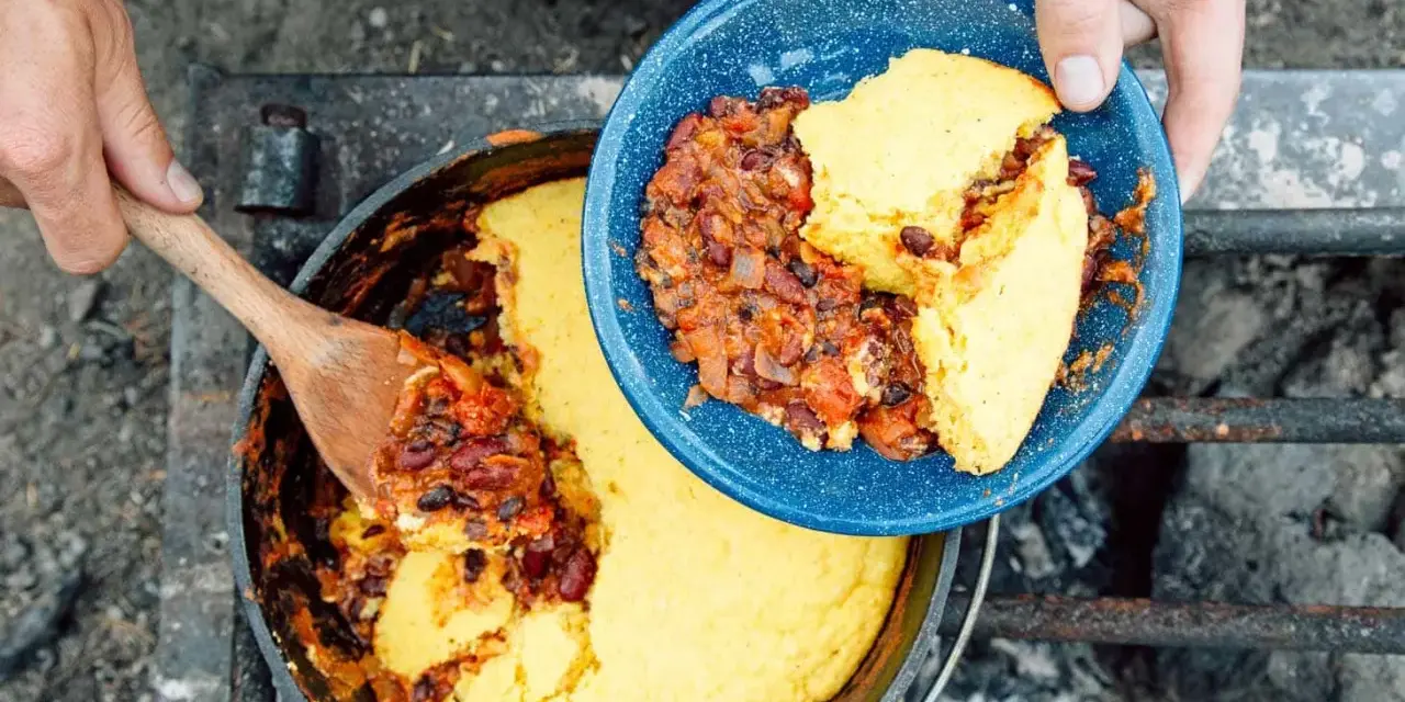 Serving hearty chili and cornbread from a Dutch oven over a campfire. This is easy camp food at its finest.