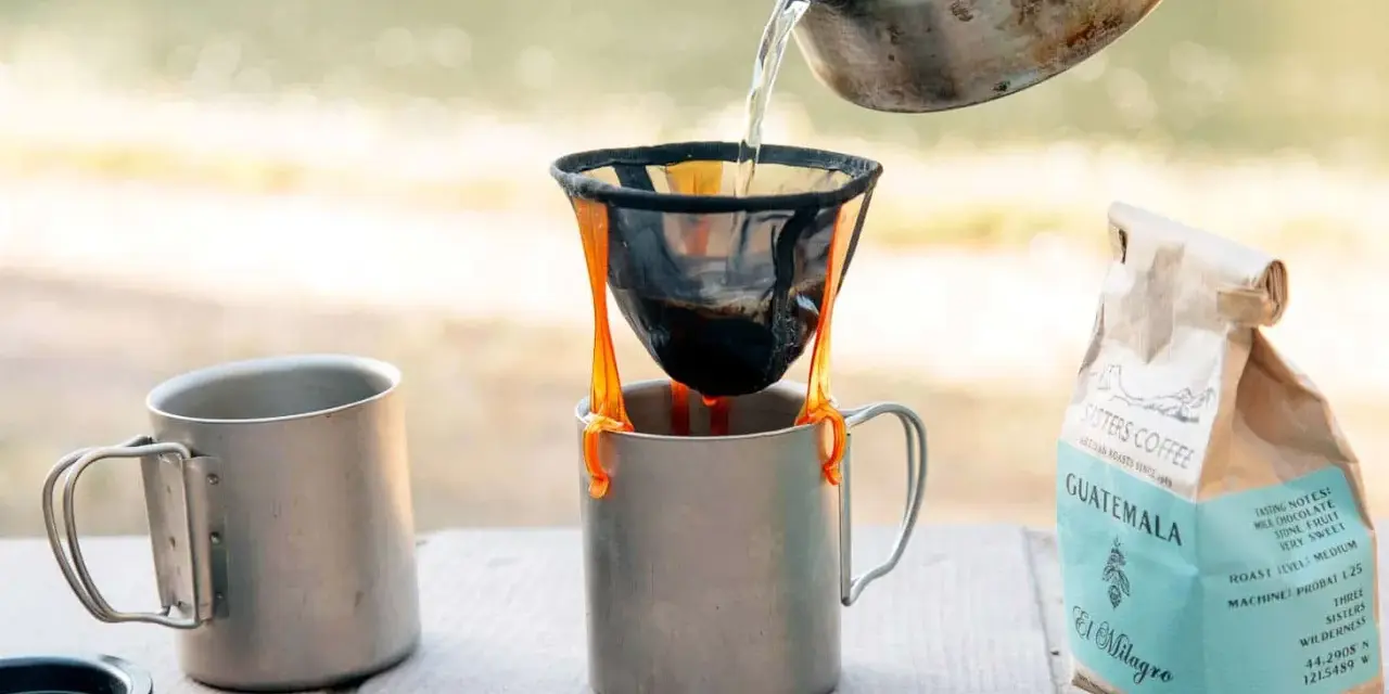 Making coffee while camping: hot water pours from a kettle into a pour-over filter, brewing coffee into a metal mug. A bag of Sisters Coffee Guatemala sits nearby.