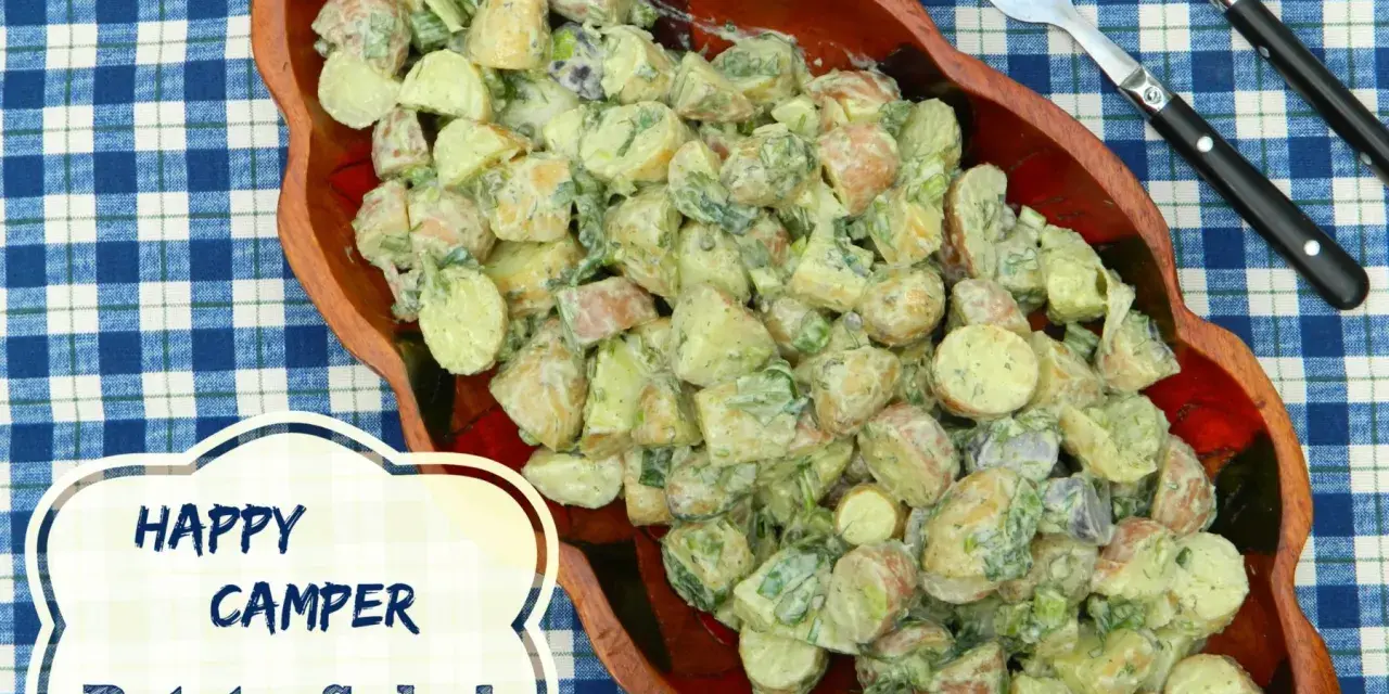 A hearty potato salad, perfect for happy campers, is served in a wooden bowl on a blue checkered tablecloth.