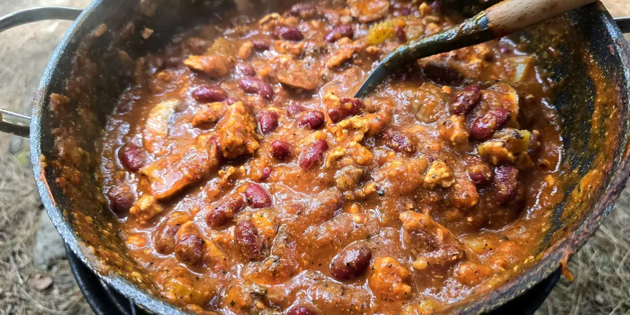 A hearty dutch oven chilli, bubbling and steaming, with kidney beans and chunks of meat, ready to be served.
