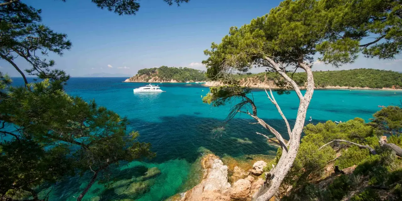 A luxury yacht sails on turquoise waters near a scenic coastline, perfect for a 3-star camping trip in Var.