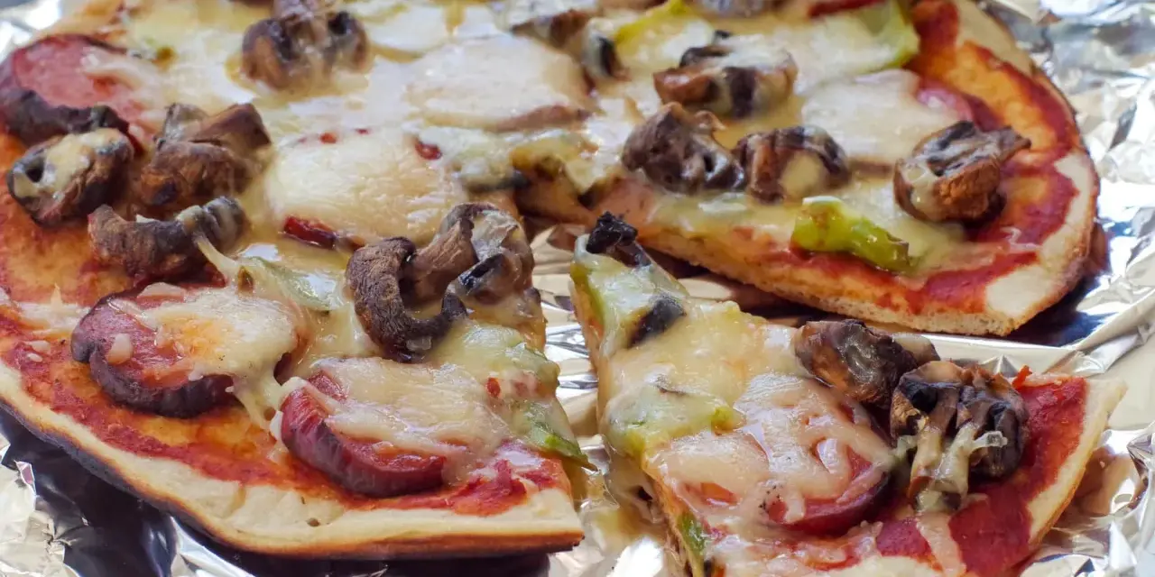 Delicious grilled pizza ideas: a pizza with mushrooms, sausage, and melted cheese on foil.
