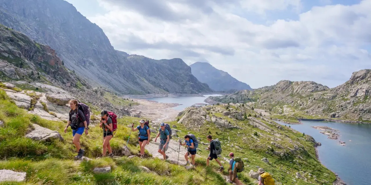 Hikers trek through a scenic mountain landscape, enjoying hiking the Pyrenees Spain. A chain of lakes and rugged peaks stretch into the distance under a cloudy sky.