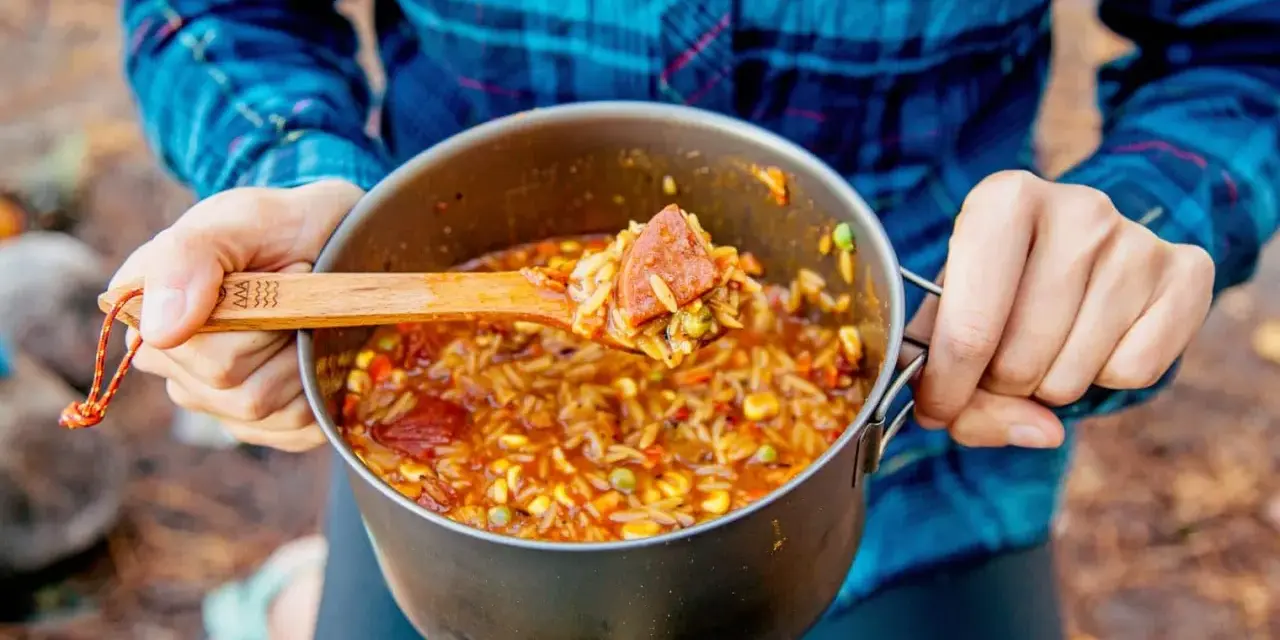 A wooden spoon scoops a hearty portion of campfire jambalaya from a pot.