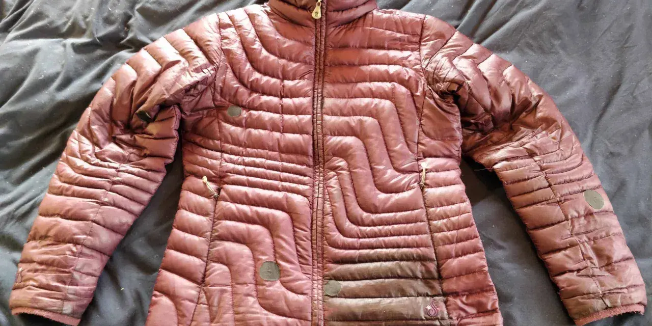A maroon puffer jacket lies on a dark, wrinkled surface, ready for cleaning. Learn how to wash a down jacket to keep it fluffy and warm.