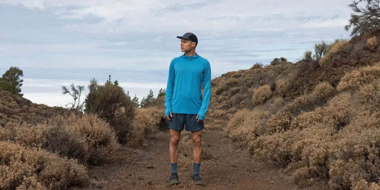 Runner in blue shirt and shorts on a dusty trail, contemplating the disadvantages of merino wool, like its tendency to hold moisture in humid conditions.