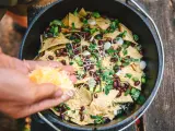Making delicious camping nachos in a Dutch oven, adding shredded cheese to tortilla chips, black beans, and green onions.