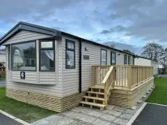 A beige Swift Provence mobil home with a wooden deck and steps. This idyllic location in Provence offers a cozy getaway.