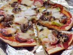 Delicious grilled pizza ideas: a pizza with mushrooms, sausage, and melted cheese on foil.