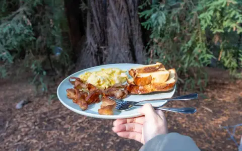 A plate of scrambled eggs, crispy bacon, and toasted bread, a delicious breakfast showcasing some great camping hacks for enjoying a hearty meal outdoors.