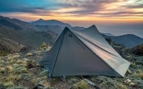 A Gossamer Gear tent sits on a rocky mountain ridge at sunset. This review highlights the gear's performance.