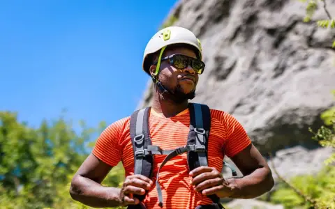 A man in a helmet and sunglasses pauses during a hike in hot weather, ready for his next climb.
