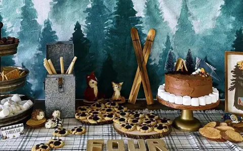 Woodland-themed camping party ideas: a chocolate cake with marshmallow border, s'mores supplies, cookies, and woodland creature decorations.