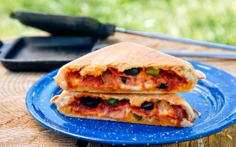 A delicious pie iron pizza, cut in half and stacked, reveals melted cheese, pepperoni, olives, and peppers.