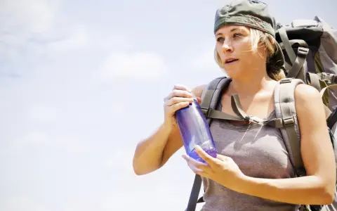 A hiker with a backpack holds a water bottle, demonstrating how to carry water while hiking.