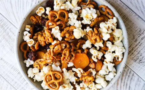 A bowl of delicious walnut trail mix, featuring popcorn, pretzels, dried cranberries, and apricots.