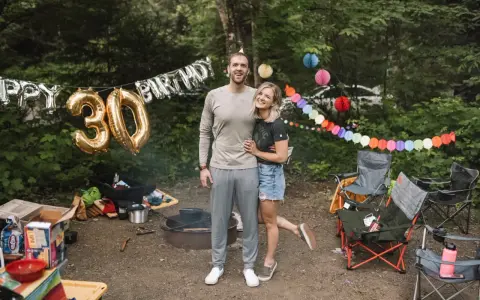 Couple celebrates 30th birthday with fun camping birthday ideas. Balloons and colorful banners decorate the campsite.