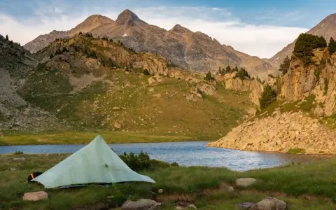 A tent sits by a serene lake, with rugged mountains in the background, a perfect campsite on the Pyrenees High Route.