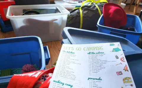 A "Let's Go Camping" checklist is spread out among blue and white storage bins, ready for a trip.