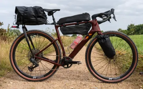 A maroon gravel bike with a full bikepacking setup, including saddle and frame bags, ready for an adventure on a dirt path.