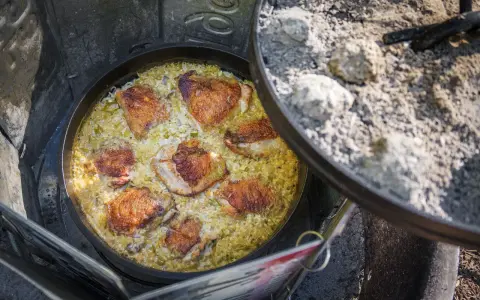 A delicious chicken and rice dish is cooking in a Dutch oven over a campfire, perfect for outdoor dutch oven campfire recipes.