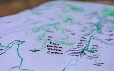 A topographic map of Zion Canyon shows elevation changes with contour lines, highlighting trails, visitor centers, and campgrounds.