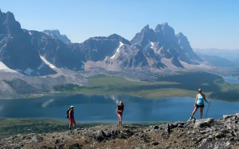 Three hikers enjoy a breathtaking view during their Tonquin Valley hike, with a stunning blue lake and jagged mountains behind them.