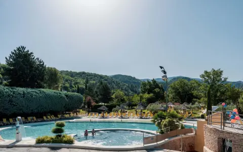 Enjoying a refreshing dip in the pool during a camping trip in Provence. Lush green hills and trees surround the sparkling water, with sun loungers and umbrellas ready for relaxation.