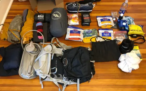 Gear laid out for beginner backpacking: tent, sleeping bag, backpack, water filter, food, and a medical kit.