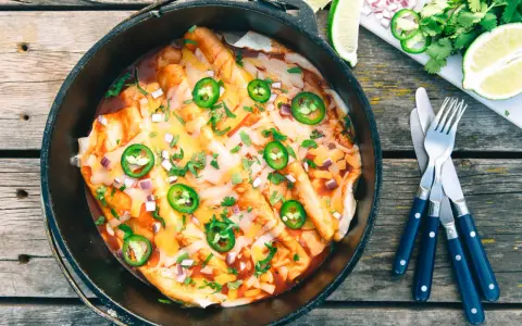 Delicious dutch oven enchiladas, topped with melted cheese, jalapeños, and cilantro, ready to be served.