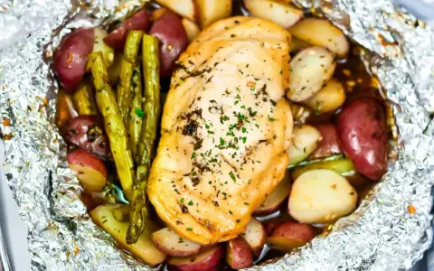 Campfire chicken foil packets in oven, with roasted potatoes and asparagus, seasoned with herbs.