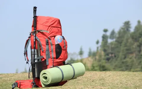 A red backpack with a rolled sleeping pad strapped to it, and trekking poles. This image shows how to pack a backpacking pack for an adventure.