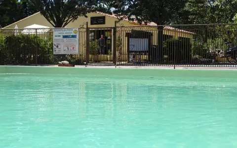 A refreshing pool awaits at this camping in Aix en Provence. A sign details pool depths, and a man stands near the reception building.