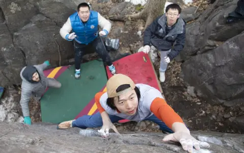 Four friends enjoy bouldering, a type of rock climbing, on a rocky outdoor course with crash pads.