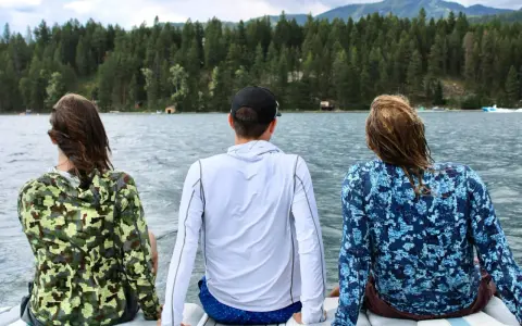 Three friends enjoy a lake view, wearing cooling clothing for extreme heat. The camouflage and blue patterned shirts offer sun protection.