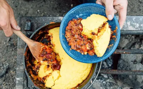 Serving hearty chili and cornbread from a Dutch oven over a campfire. This is easy camp food at its finest.