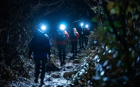 Hikers with headlamps navigate a dark, rocky trail, illuminated by their lights. These are some of the best night hiking tips.