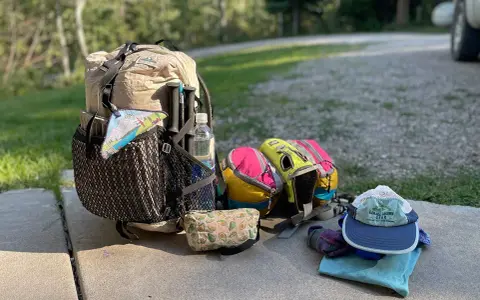 Ready for adventure! This ultralight backpacking gear list includes a tan pack, colorful stuff sacks, trekking poles, a water bottle, and a hat.