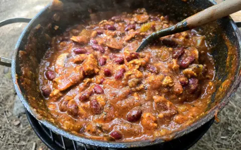 A hearty dutch oven chilli, bubbling and steaming, with kidney beans and chunks of meat, ready to be served.
