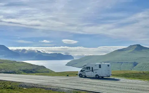 A white RV parked on a scenic road overlooking a bay and green mountains. This view is perfect for the best RV trip planner.