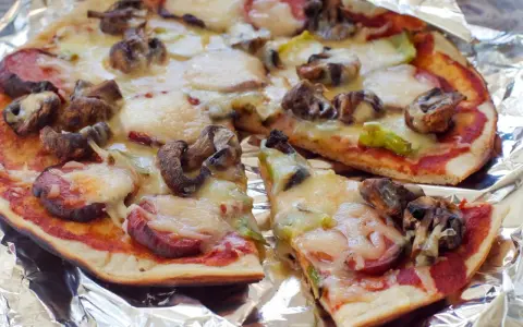 Delicious grilled pizza ideas: a pizza with mushrooms, sausage, and melted cheese on foil.