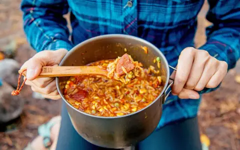 A wooden spoon scoops a hearty portion of campfire jambalaya from a pot.